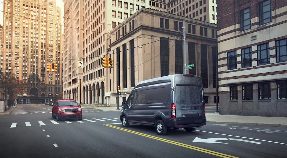 A gray 2023 Ford Transit is shown driving on a city street.