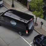 A black 2023 Ford Transit is shown reversing onto a parking spot.