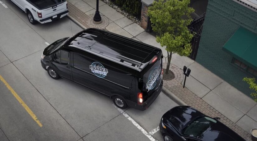 A black 2023 Ford Transit is shown reversing onto a parking spot.