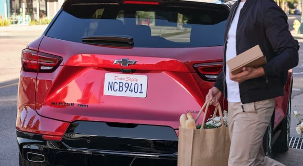 A red 2024 Chevy Blazer is shown parked near a person holding a bag.