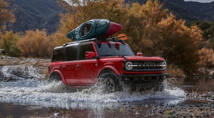 A red 2024 Ford Bronco Outer Banks for sale is shown fording a river.