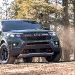 A green 2024 Ford Explorer Timberline is shown driving in a forest after visiting a Ford dealer.