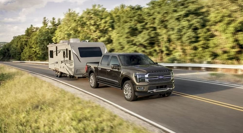 A black 2024 Ford F-150 Platinum is shown towing a camper on a highway.