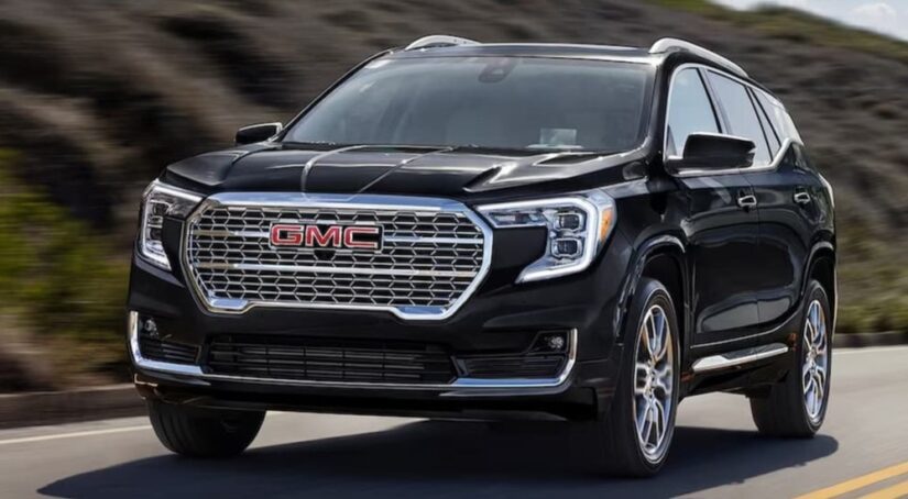 A popular GMC Terrain for sale, a black 2024 GMC Terrain, is shown driving on a highway.