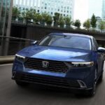 A blue 2024 Honda Accord Touring Hybrid is shown driving on a city street.