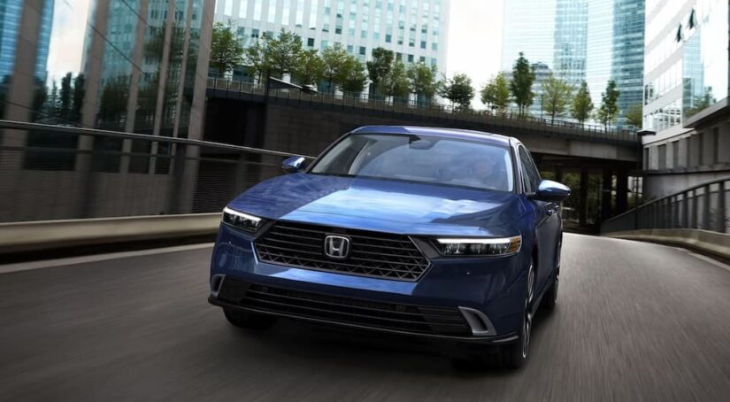 A blue 2024 Honda Accord Touring Hybrid is shown driving on a city street.