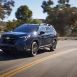A blue 2024 Subaru Ascent for sale is shown driving on a highway.