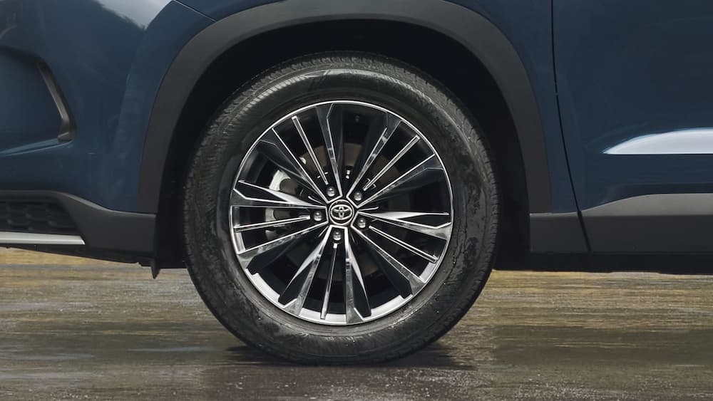A close-up of a wheel on a blue 2024 Toyota Grand Highlander is shown.
