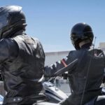 Three people are shown wearing helmets near a motorcycle dealer.