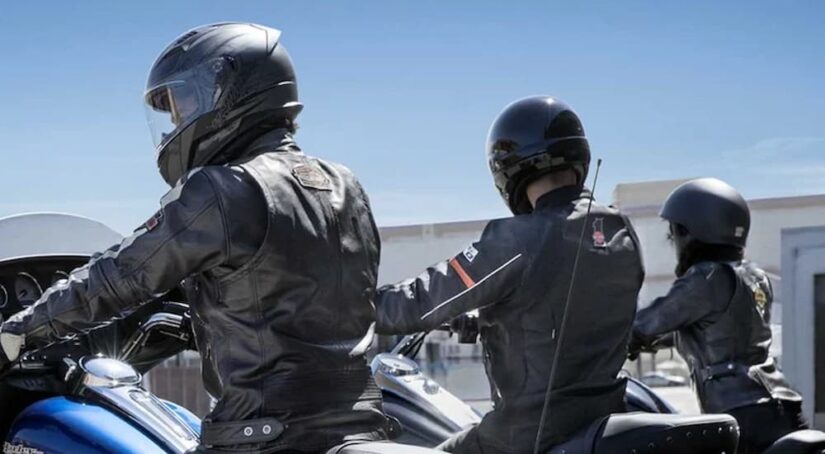 Three people are shown wearing helmets near a motorcycle dealer.
