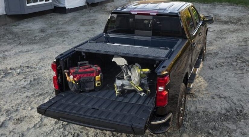 A hard folding painted Tonneau cover is shown on the bed of a black Chevy truck.