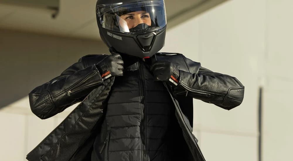 A person is shown wearing a Harley-Davidson helmet and adjusting her jacket.