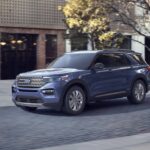 One of many used SUVs for sale, a blue 2020 Ford Explorer, is shown driving near a building.