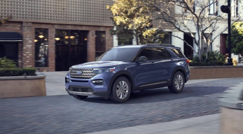 One of many used SUVs for sale, a blue 2020 Ford Explorer, is shown driving near a building.