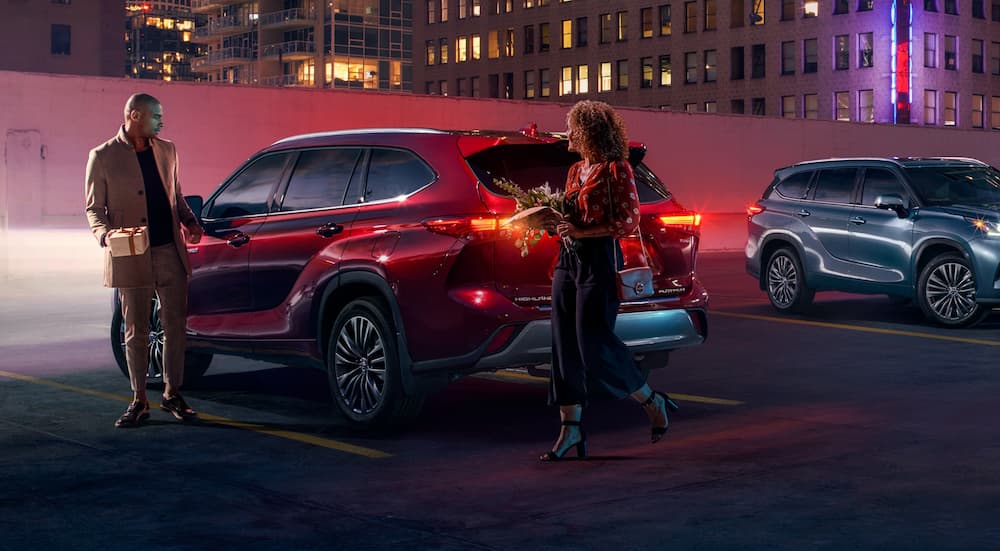 A red 2020 Toyota Highlander Hybrid is shown parked near two people.
