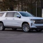 A white 2021 Chevy Suburban is shown parked in a city near a used Chevy dealer.