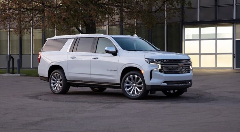 A white 2021 Chevy Suburban is shown parked in a city near a used Chevy dealer.