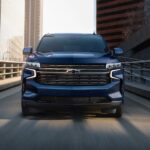 A blue 2023 Chevy Tahoe for sale is shown driving on a bridge.
