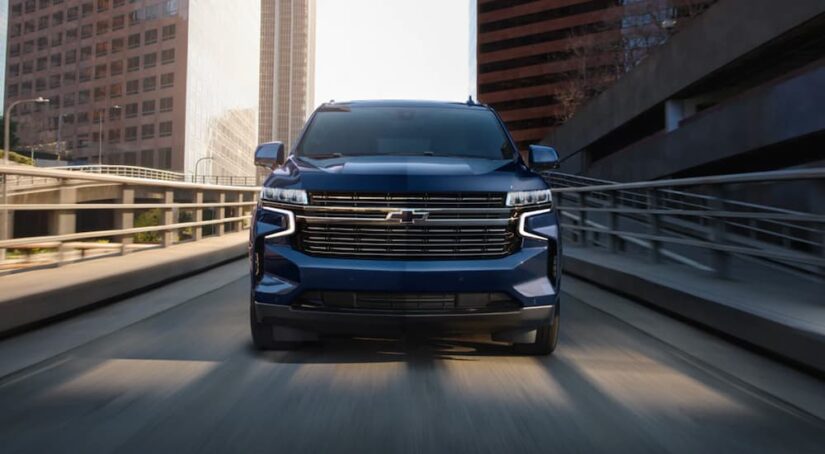 A blue 2023 Chevy Tahoe for sale is shown driving on a bridge.