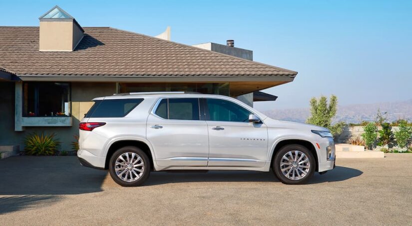 A white 2023 Chevy Traverse is shown parked near a house after viewing several used Chevy SUVs for sale.