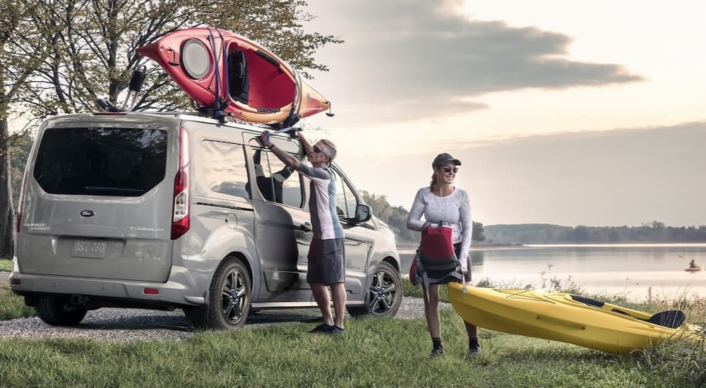Two people are shown unloading kayaks from a silver 2023 Ford Transit Connect Passenger Wagon.