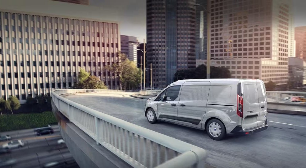 A white 2023 Ford Transit Connect Cargo Van is shown driving near a city.