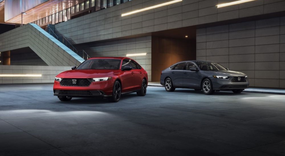 A red 2023 Honda Accord Sport L Hybrid LX and a grey 2023 Honda Accord Sport L Hybrid LX are shown parked in a garage.