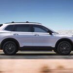 A white 2023 Honda CR-V Sport Touring Hybrid is shown driving on a desert road after visiting a Honda dealer.