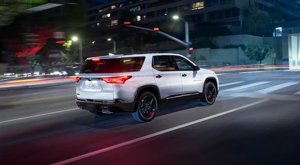 A white 2023 Chevy Traverse is shown driving on a city street at night.
