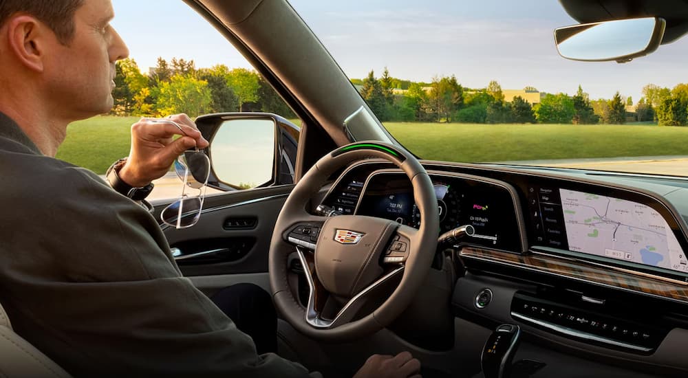 The black interior of a 2024 Cadillac Escalade is shown with a person seated in the drivers seat.