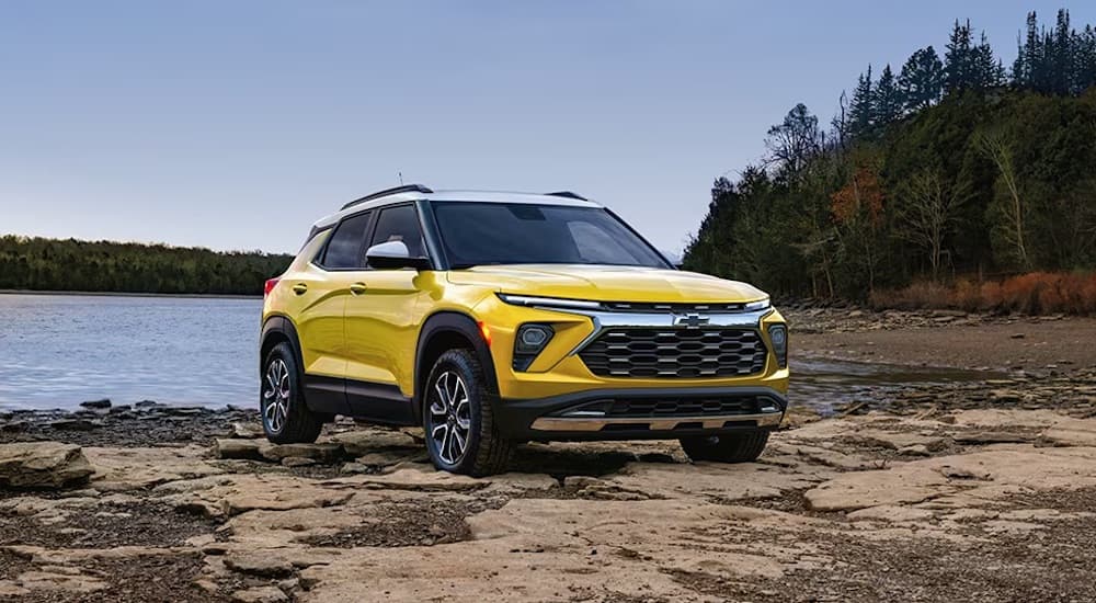 A yellow 2024 Chevy Trailblazer is shown parked off-road near a lake.