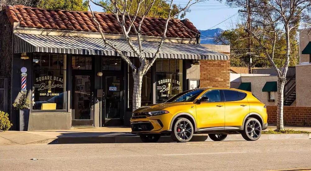 A yellow 2024 Dodge Hornet is shown parked near a barber shop.