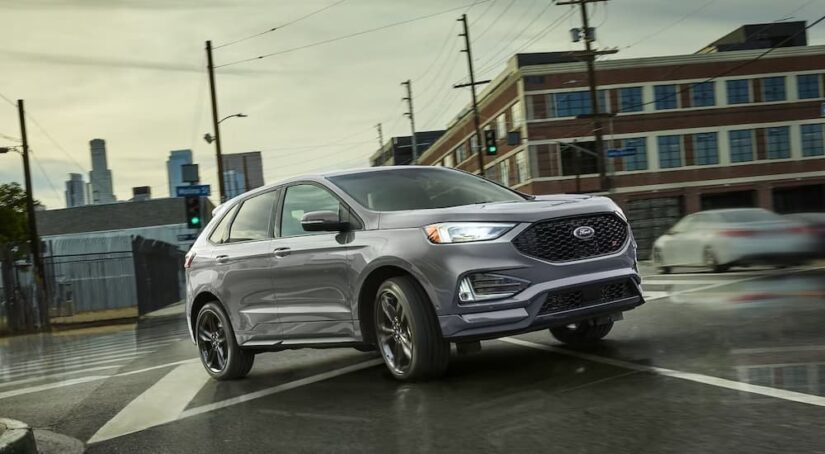 After participating in a 2024 Ford Edge vs 2024 Chevy Blazer comparison, a silver 2024 Ford Edge ST, is shown driving on an intersection.