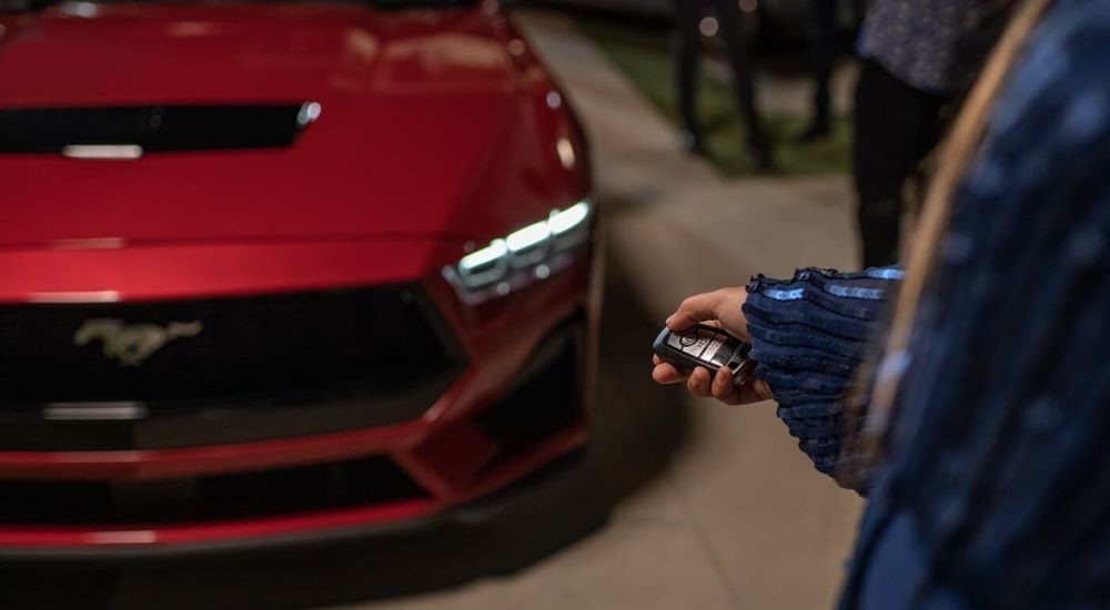 A person is shown locking a red 2024 Ford Mustang with a key fob.
