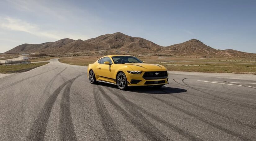 A yellow 2024 Ford Mustang parked on an empty road in front of mountains.