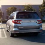 A family walking to their silver 2024 Honda Odyssey in a parking lot.