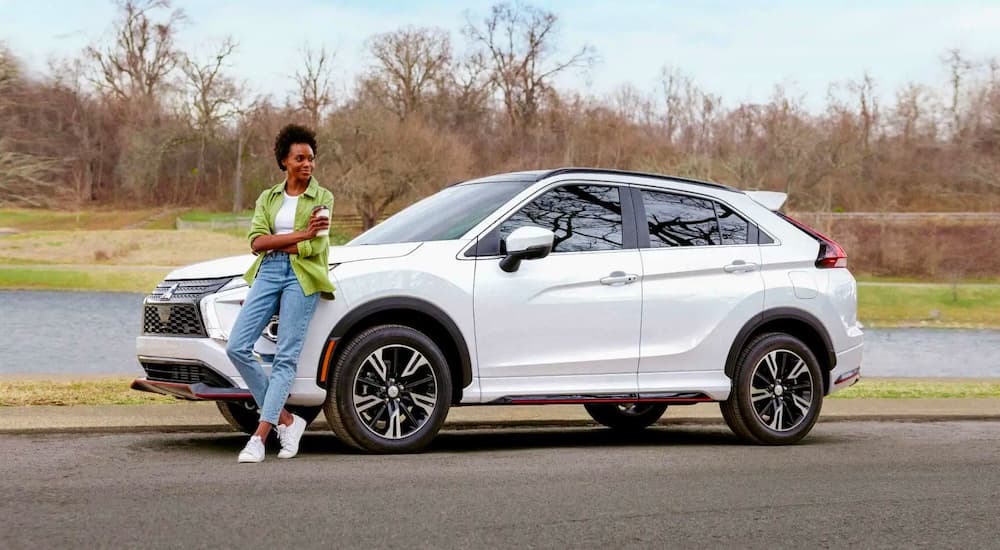 A person is shown leaning against a parked white 2024 Mitsubishi Eclipse Cross.