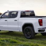 Side-view of a white 2024 GMC Sierra 1500 parked on a grassy hill.