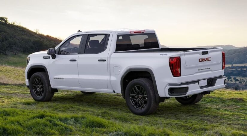 Side-view of a white 2024 GMC Sierra 1500 parked on a grassy hill.