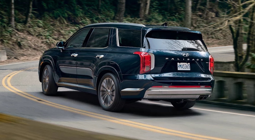 Rear view of a blue 2025 Hyundai Palisade driving from a Hyundai dealer.