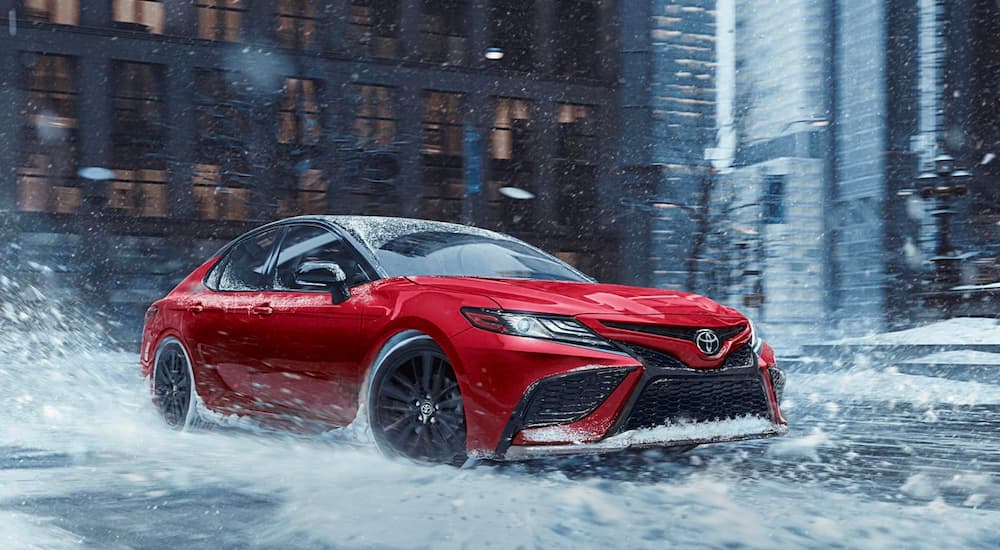 A red 2020 Toyota Camry is shown driving through a city.