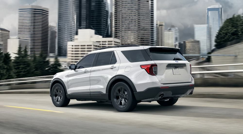 A white 2021 Ford Explorer is shown driving on a city street near buildings.