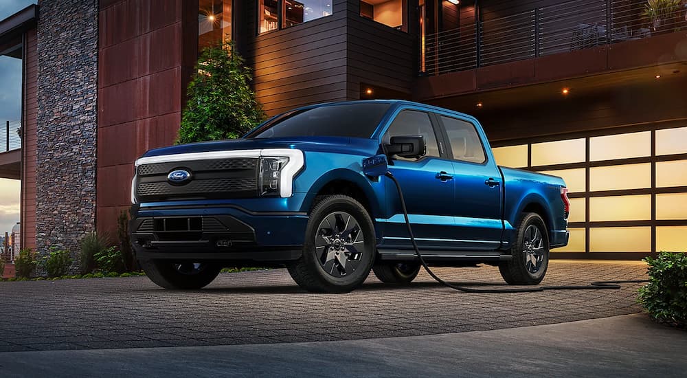 A blue 2022 Ford F-150 Lightning is shown charging in a driveway.