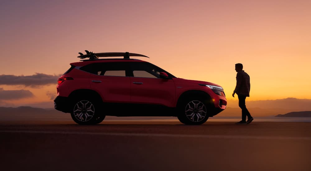 A person is shown walking towards a red 2022 Kia Seltos parked on a beach.