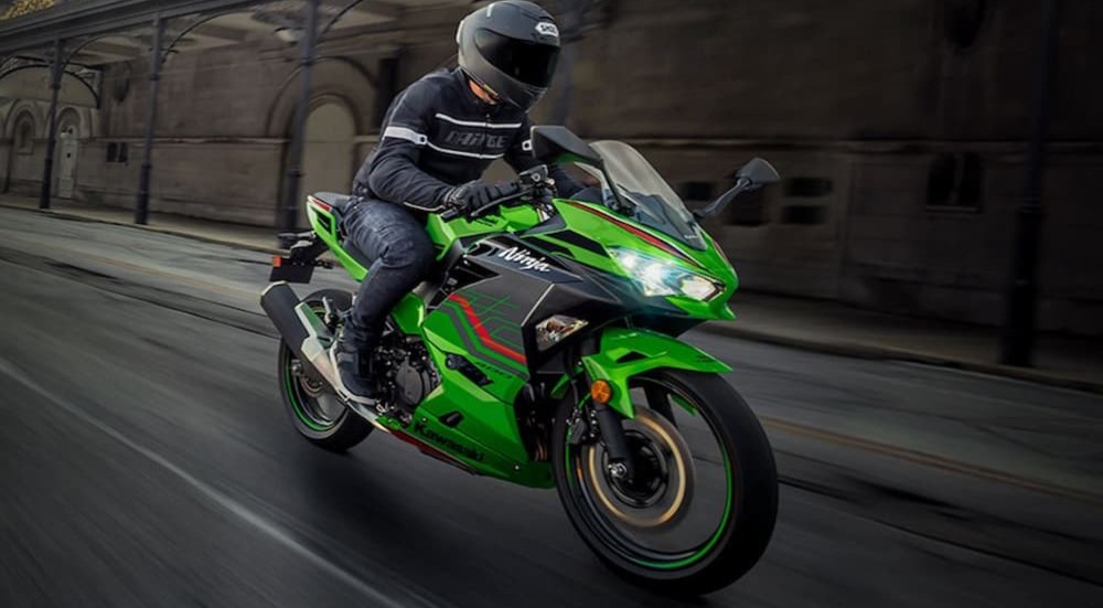 A green 2023 Kawasaki Ninja 400 is shown driving on a city street.