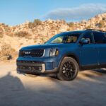 A blue 2024 Kia Telluride for sale is shown parked on sand.