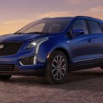 A blue 2024 Cadillac XT5 is shown parked off-road after visiting a Cadillac dealer.