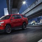 A red 2024 Chevy Tahoe is shown driving on a city street.