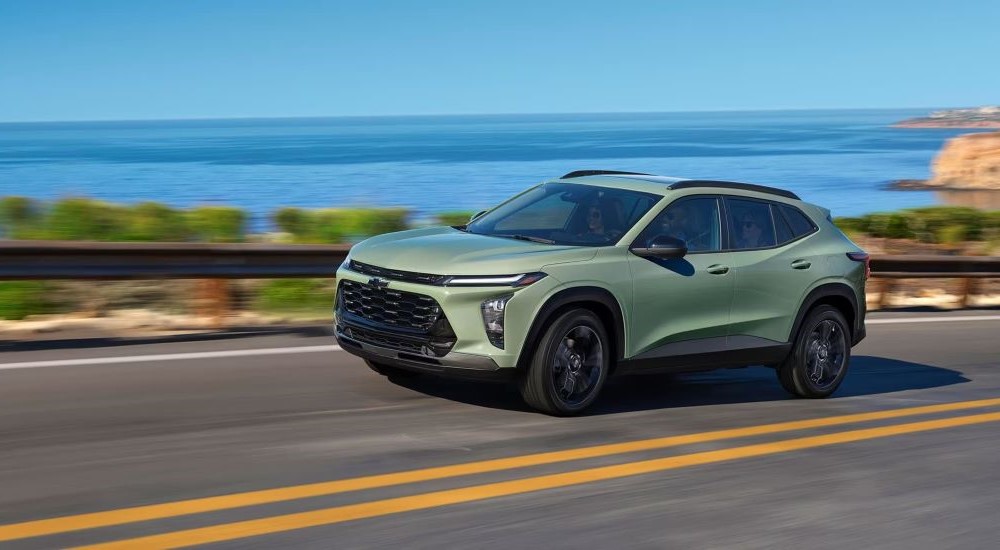 A pale green 2024 Chevy Trax driving on a coastal road overlooking the ocean.