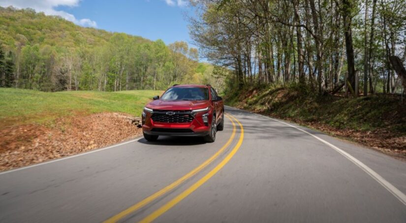 A red 2024 Chevy Trax RS driving toward the camera on a tree-lined road.